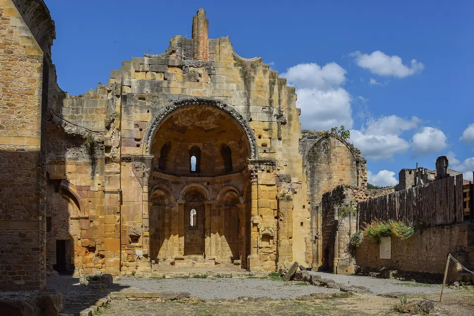 Ruines d'une grande église romane en pierre dorée, avec une abside percée de fenêtres et des murs sans toit, sous un ciel bleu