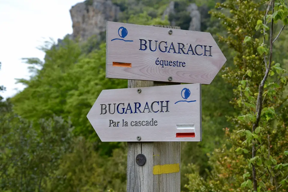 Deux panneaux de direction en bois indiquant Bugarach, l'un pour le parcours équestre, l'autre par la cascade, devant une falaise boisée