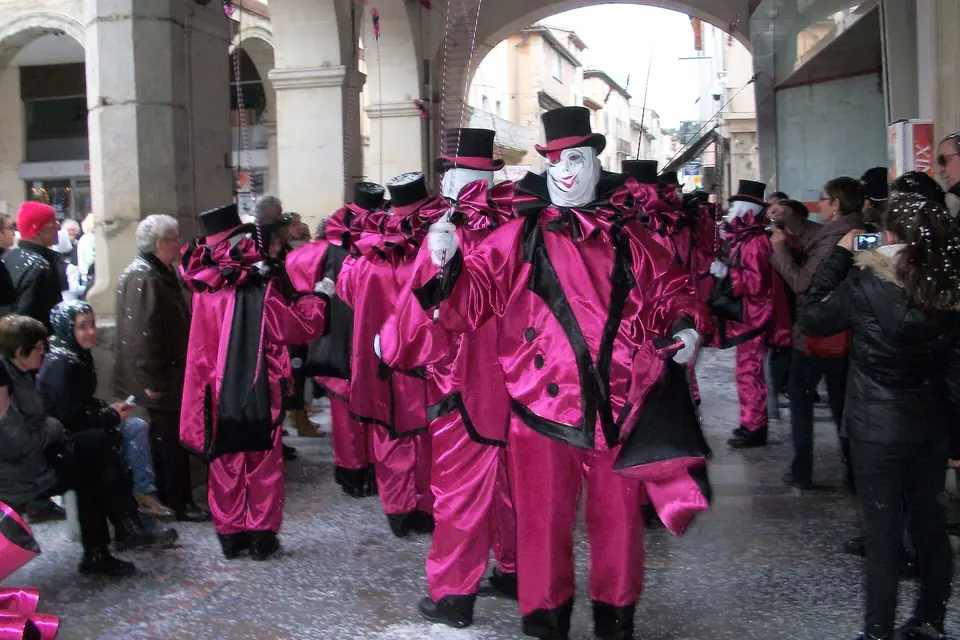 Une bande de carnavaliers masqués en costume de satin fuchsia et chapeau haut de forme dansant sous des arcades, devant une foule de spectateurs