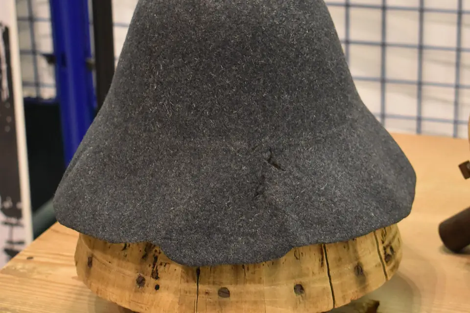 Une cloche de feutre gris en forme de chapeau pointu posée sur une forme en bois, dans une salle de musée