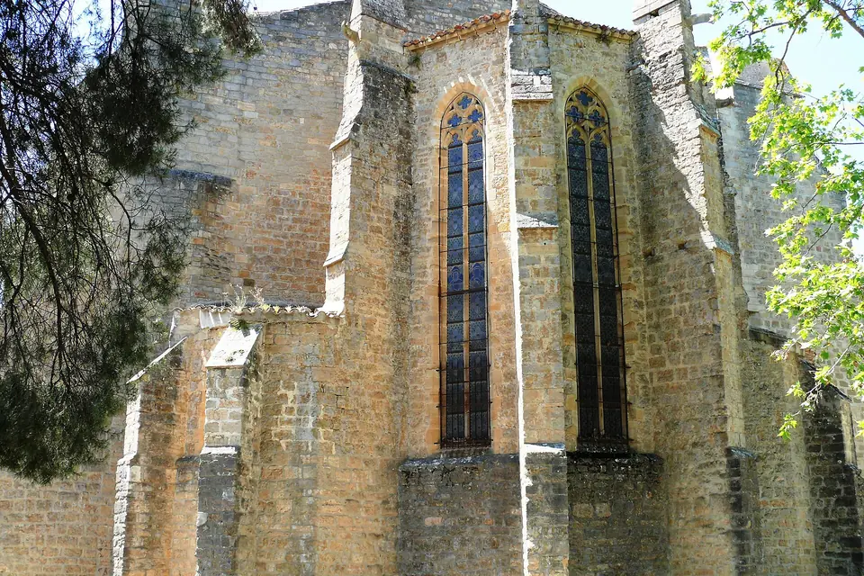 Chevet gothique en pierre blonde d'une église, percé de hautes fenêtres à remplages, entouré d'arbres